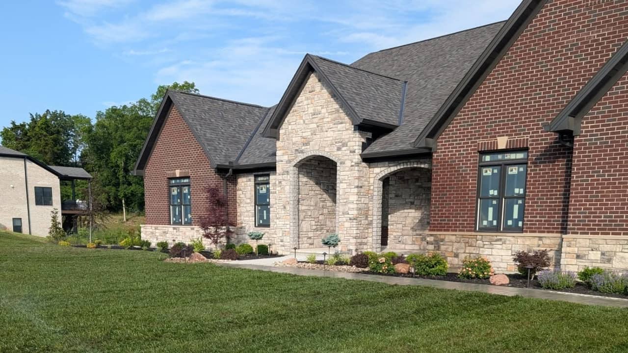 Sprinkler head watering a green lawn in front of the same stone and brick home in daylight.