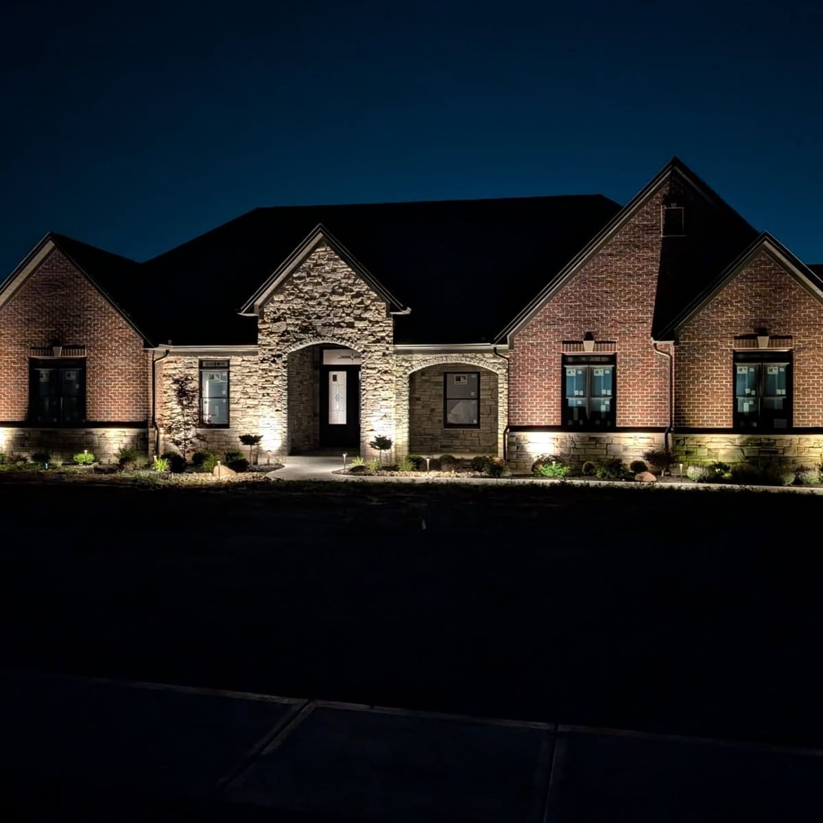 Side elevation of a brick home uplit against a deep blue dusk sky.
