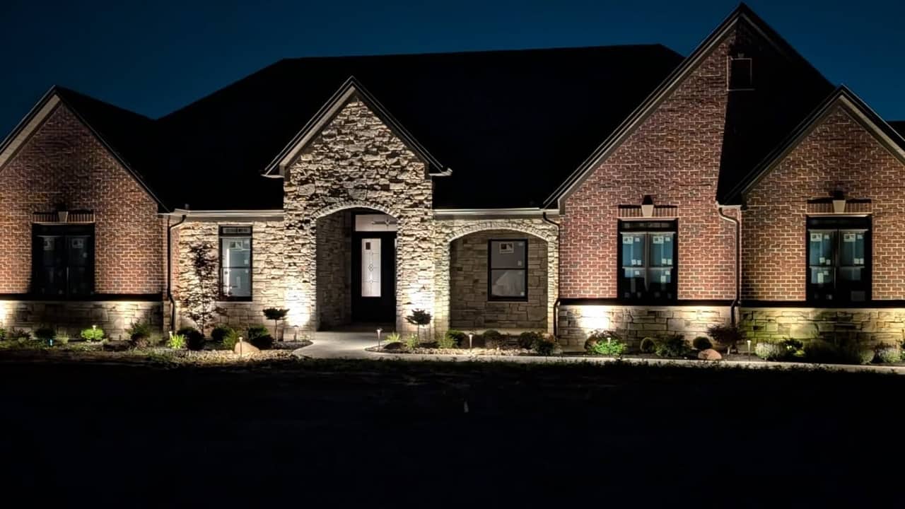 Side elevation of a brick home uplit against a deep blue dusk sky.