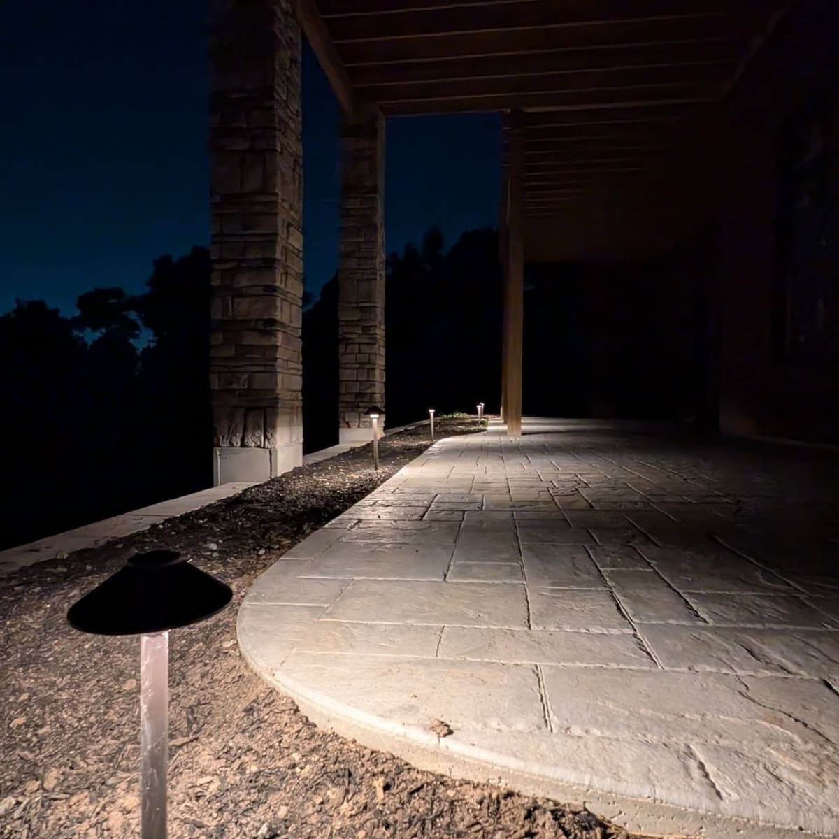 Path lights along a stamped concrete patio under a covered porch at night.