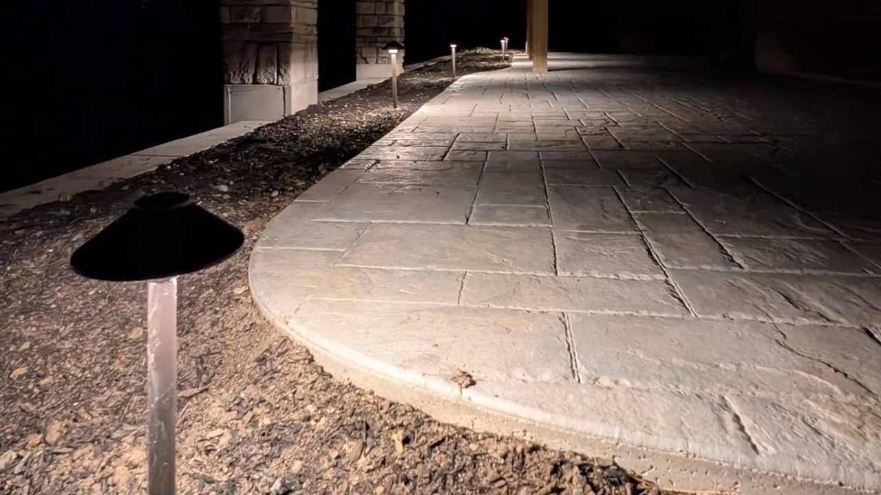 Path lights along a stamped concrete patio under a covered porch at night.