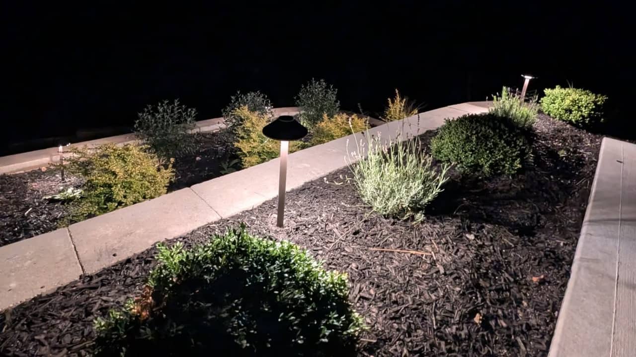 Low path lights lining a sidewalk beside a planting bed in the evening.