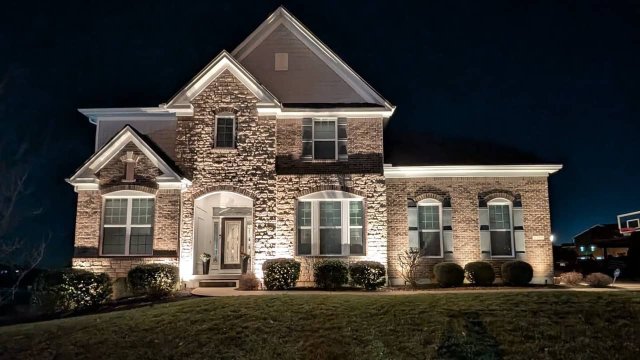Stone and brick ranch home washed with warm uplighting at dusk, path lights along the front beds.